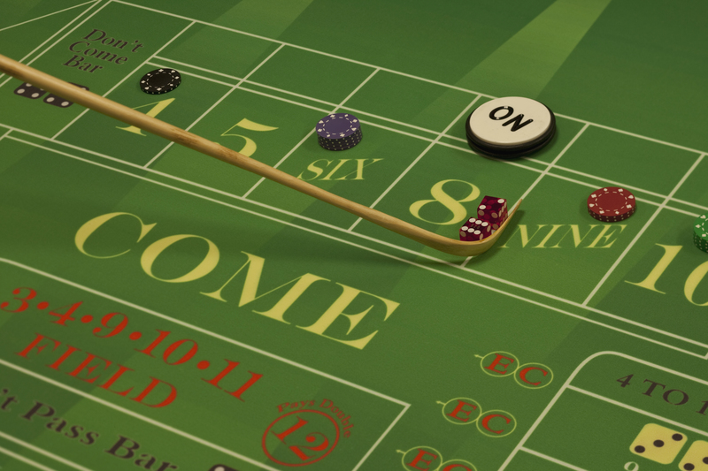 A close-up of a green craps table featuring dice, betting chips, and a stick indicating a recent bet.