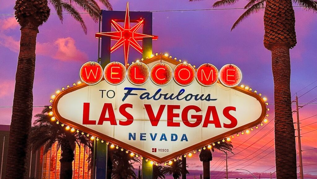 The "Welcome to Fabulous Las Vegas" neon sign framed by palm trees against a vibrant purple and orange sunset sky.