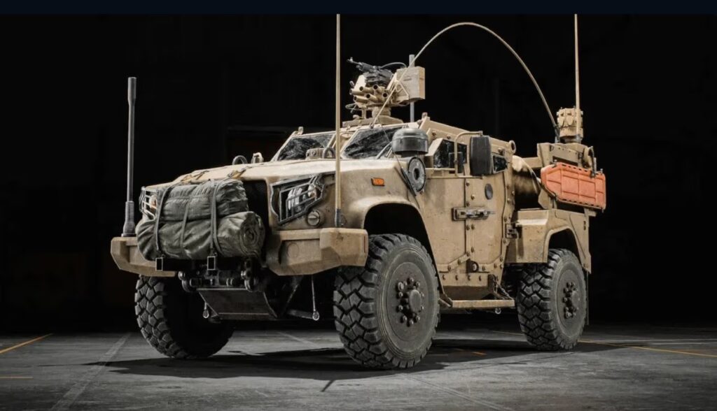 A side-profile view of the new NATO LTV armored vehicle in a dark garage, featuring a mounted machine gun and tactical gear.