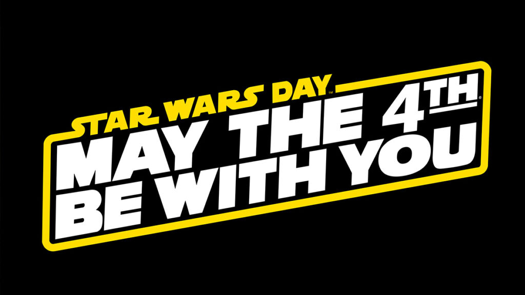 A logo with "STAR WARS DAY" in small yellow text above the large white block letters "MAY THE 4TH BE WITH YOU," all enclosed in a yellow-bordered slanted banner on a black background.